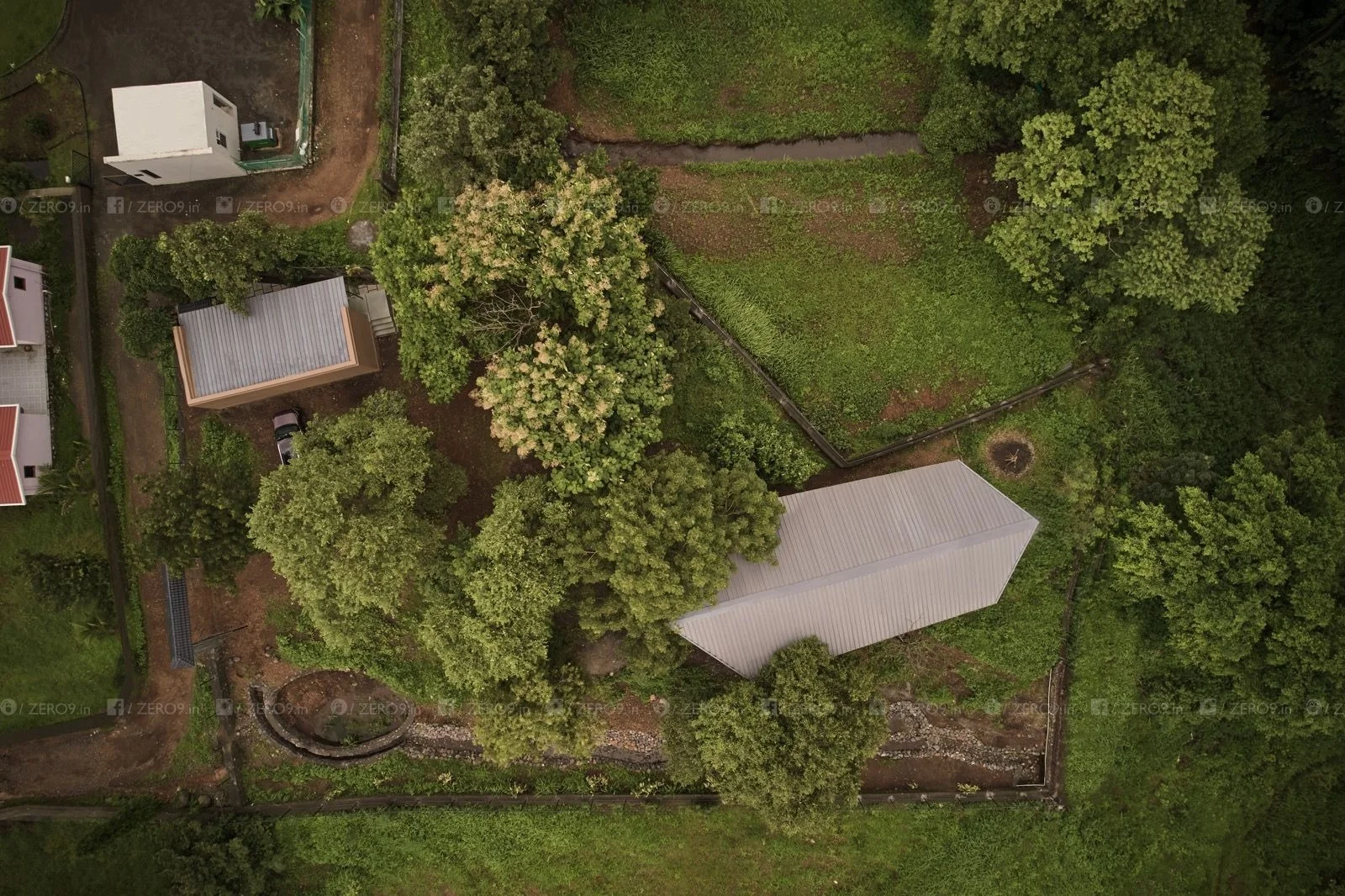 Top-down aerial of the half-acre plot — the stone-lined stream weaves along the boundary, the compact farmPAD footprint preserving the surrounding dense vegetation